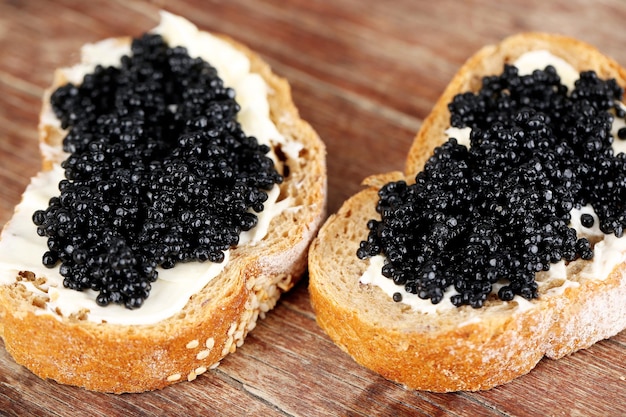 Rebanadas de pan con mantequilla y caviar negro sobre fondo de madera