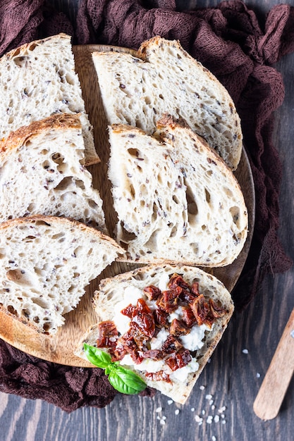 Rebanadas de pan con ricotta, tomates secados al sol y albahaca servidos en tabla de cortar de madera. Bruschetta con ricotta, tomates secos y albahaca.