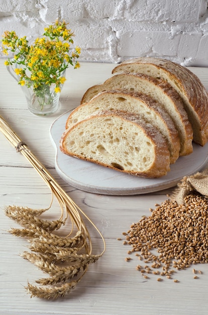 Rebanadas de pan sobre tabla de cortar y espiguillas de trigo sobre fondo de pared blanca Estilo rústico