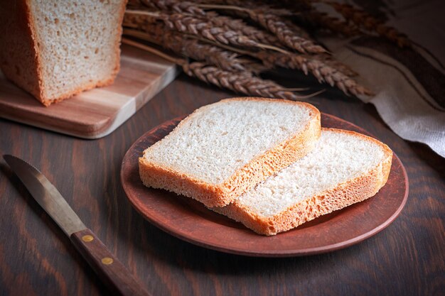 Rebanadas de pan de trigo casero servido en un plato sobre una mesa de madera de color marrón oscuro con cultivo de granos