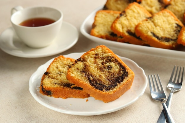 Rebanadas de pastel Bundt de mármol en plato blanco, servido con una taza de té