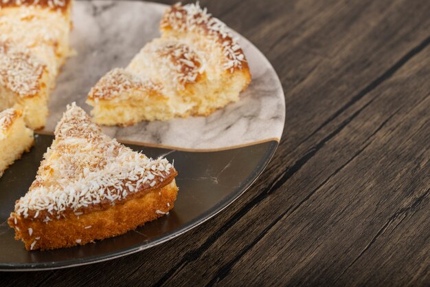 Rebanadas de pastel de postre con virutas de coco colocadas sobre una mesa de madera.