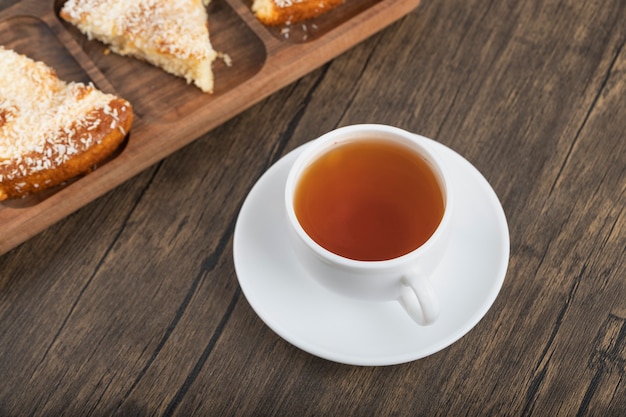 Rebanadas de pastel de postre con virutas de coco y taza de té colocados sobre una mesa de madera.