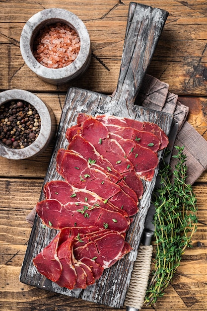 Rebanadas de pastrami seco, carne de vacuno con hierbas sobre tabla de madera. Fondo de madera. Vista superior.