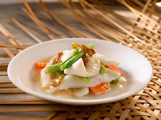 Rebanadas de pescado San Yu con cebolleta y jengibre servido en un plato aislado en la vista lateral de la mesa