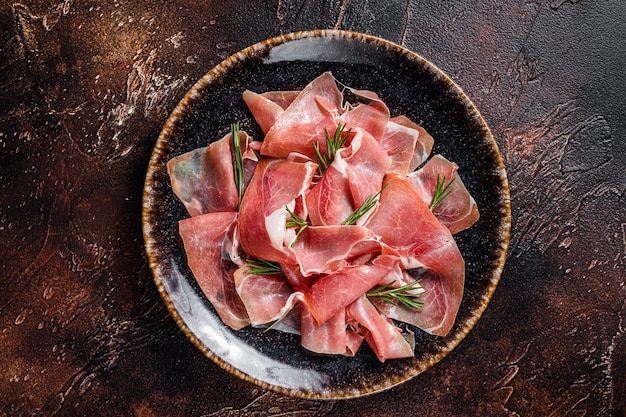 Rebanadas de prosciutto crudo parma o jamón serrano con romero. Fondo oscuro. Vista superior.