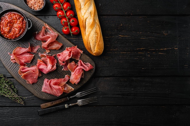 Rebanadas de prosciutto di parma o jamon serrano sobre fondo de madera negra vista superior plana con espacio de copia para texto