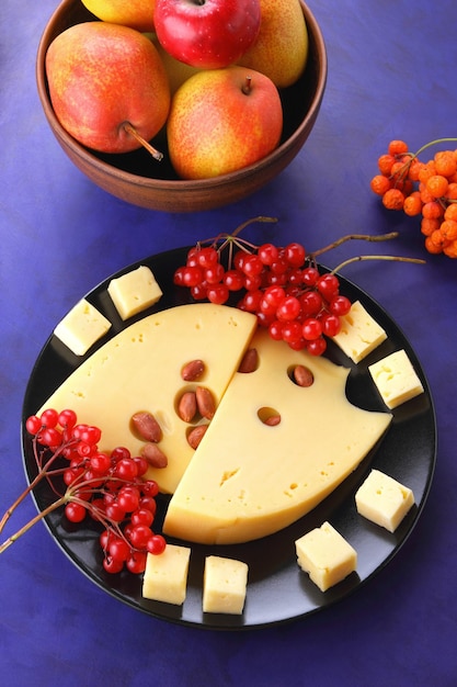 Rebanadas de queso amarillo duro con nueces y bayas en un plato negro sobre un fondo azul Primer plano de lonchas de queso duro con grandes agujeros Vista desde arriba