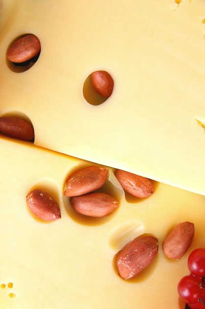 Rebanadas de queso amarillo duro con nueces y bayas en un plato negro sobre un fondo azul Primer plano de rebanadas de queso duro con agujeros grandes