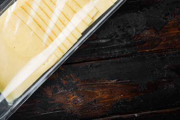 Rebanadas de queso americano en paquete de plástico, sobre fondo de madera oscura con espacio para copiar texto