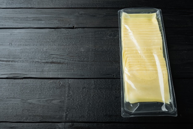 Rebanadas de queso americano en paquete de plástico, sobre mesa de madera negra con espacio para copiar texto