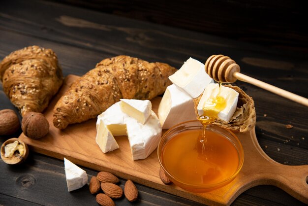 Rebanadas de queso brie o camembert con croissants, miel y nueces a bordo para cortar, sobre fondo de madera oscura.