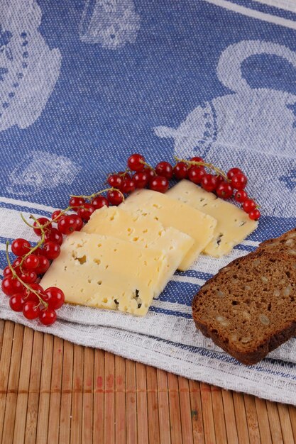 Rebanadas de queso duro amarillo con grosellas rojas pepino y pan de grano en una servilleta azul Primer plano de un refrigerio saludable Concepto de comida saludable