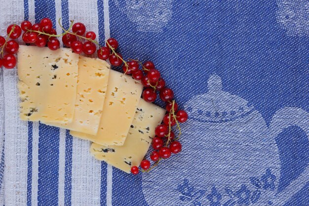 Rebanadas de queso duro amarillo y grosellas rojas en una servilleta azul Primer plano de un refrigerio saludable Concepto de comida saludable Vista desde arriba