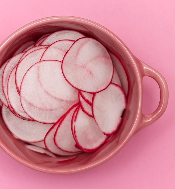 Foto rebanadas de rábanos en un cuenco rosado sobre un fondo rosado