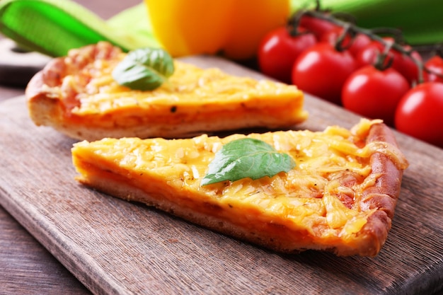 Rebanadas de sabrosa pizza de queso con albahaca y verduras en la mesa de cerca