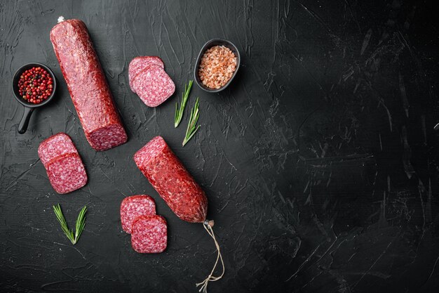 Rebanadas de salami con verduras, en la mesa de piedra oscura negra, vista superior plana