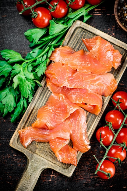 Rebanadas de salmón salado con verduras y tomates en una tabla para cortar