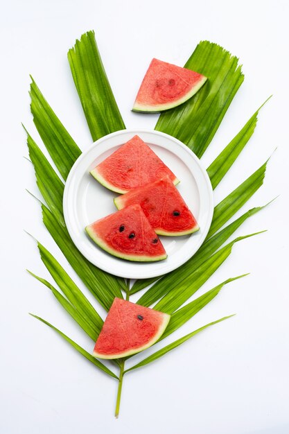 Rebanadas de sandía en hojas de palmeras tropicales en blanco