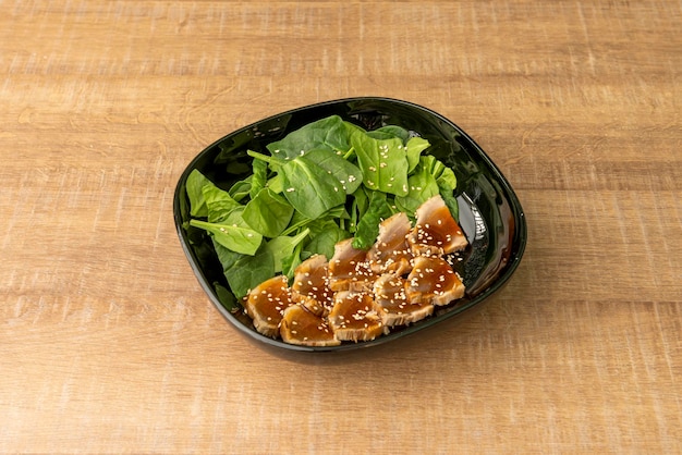 Rebanadas de tataki de atún rojo con semillas de sésamo y ensalada de espinacas dentro de un tazón negro brillante