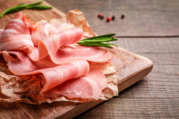 Rebanadas de tocino crudo y ramita de romero sobre tabla de cortar de madera sobre madera.