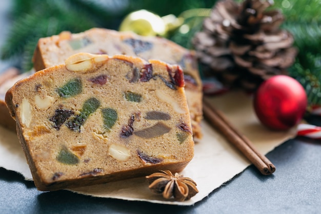 Foto las rebanadas de la torta de la fruta dulce en el papel marrón pusieron en la tabla del granito negro en visión cercana con la decoración de la navidad.