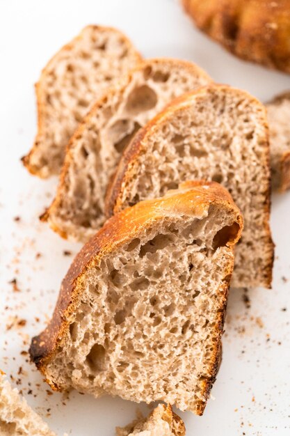 Rebanar pan de centeno de masa fermentada recién horneado en una tabla de cortar blanca