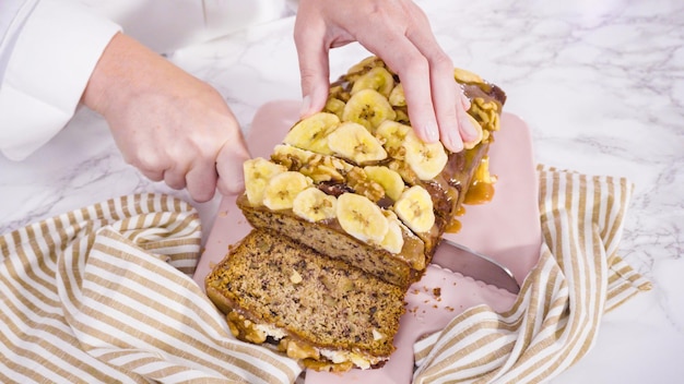 Rebanar pan de nuez de plátano cubierto con caramelo y adornado con chips de plátano y nueces.