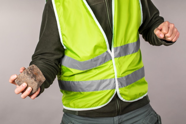 Rebell oder protestierender Arbeiter in einer gelben Weste mit einem Ziegelstein in den Händen auf grauem Hintergrund