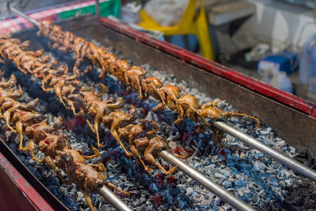 Rebhuhn oder Wachtel, die auf einer Holzkohle gegrillt werden, ist ein Grillessen vom Vogelverkauf im thailändischen Straßenlebensmittel