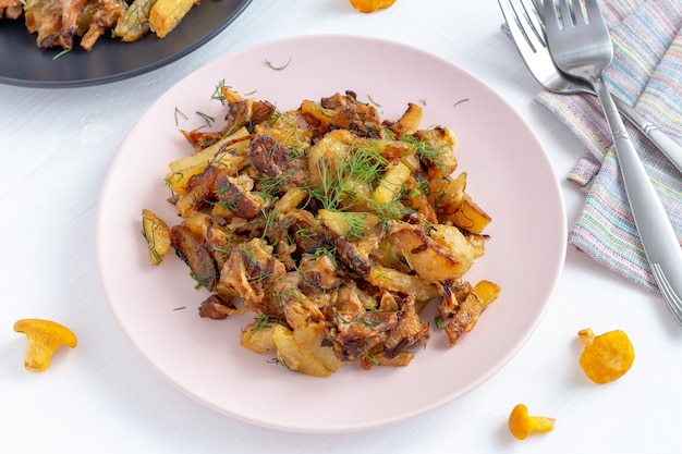 Rebozuelos del bosque fritos con patatas en un plato sobre fondo de madera blanca.