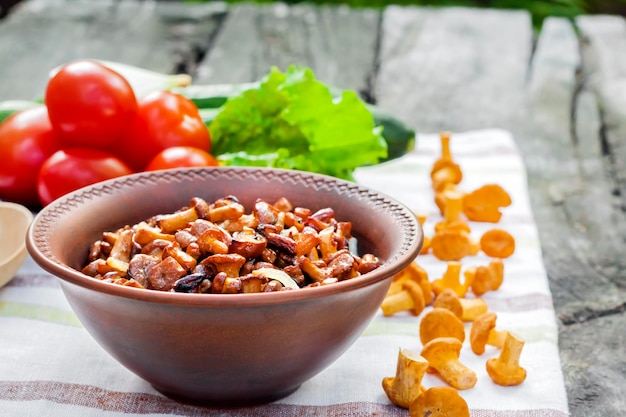 Rebozuelos fritos con cebolla en un tazón rústico y plato con verduras frescas para ensalada en el fondo