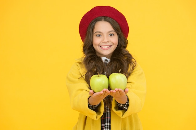 Receba vitaminas no início do ano letivo. Garota feliz segurar fundo amarelo de fruta vitamina. Sorriso de criança pequena com maçãs verdes. Lanche de vitamina saudável. Saúde escolar. Melhores fontes de vitaminas.