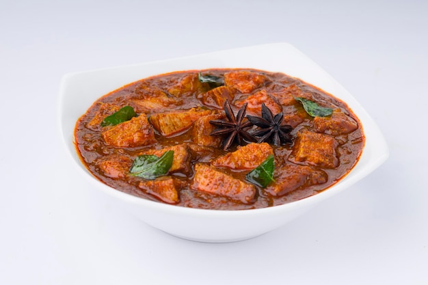 Receita caseira de masala de carne ou curry disposta em tigela branca e guarnecida com folhas de coentro e anis estrelado em fundo branco