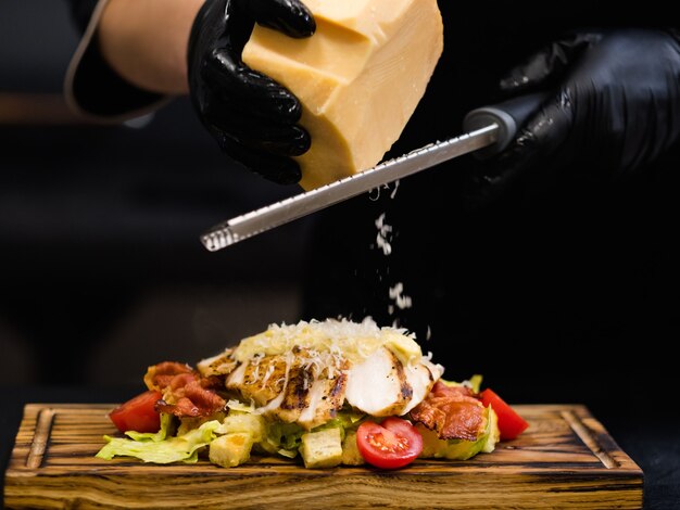 Receita tradicional italiana. foto colhida do chef ralando queijo parmesão em salada césar com filé de frango defumado e bacon.