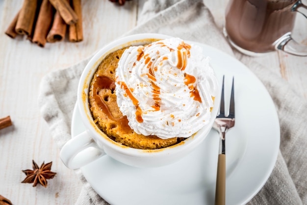 Receitas com abóboras, fast food, refeição de microondas. torta de abóbora picante em caneca, com chantilly, sorvete, canela, anis. na mesa de madeira branca, com uma xícara de chocolate quente. copie o espaço