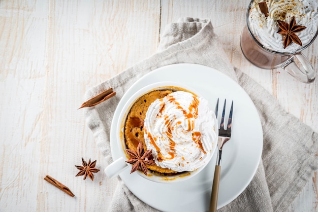 Receitas com abóboras, fast food, refeição de microondas. torta de abóbora picante em caneca, com chantilly, sorvete, canela, anis. na mesa de madeira branca, com uma xícara de chocolate quente. copyspace