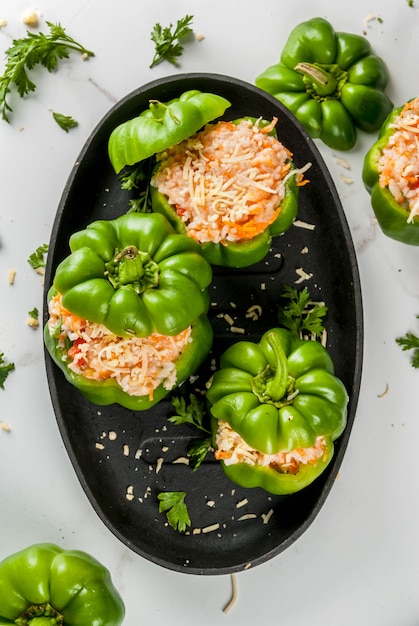 Receitas de outono. Pimentão recheado em casa com carne picada, cenoura, tomate, ervas, queijo. Processo de cozimento. Mesa de mármore branco. Pimenta recheada pronta para assar, na panela, vista superior do espaço de cópia