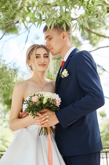 Recém-casados caminham na natureza no parque após a cerimônia de casamento. um beijo e um abraço de um homem e uma mulher