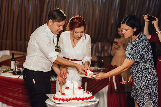 Foto recém-casados cortam alegremente, riem e provam o bolo de casamento