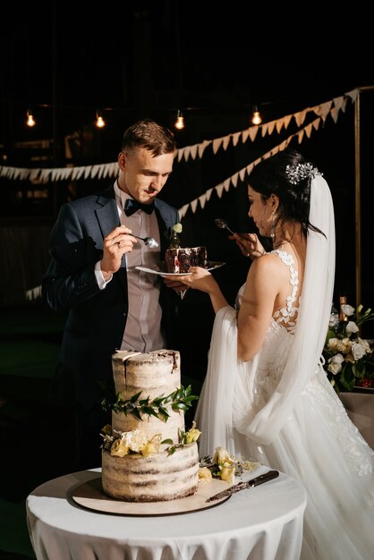 Recém-casados cortam alegremente, riem e provam o bolo de casamento
