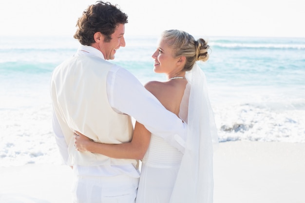 Recém-casados ​​em pé junto ao mar, sorrindo um para o outro