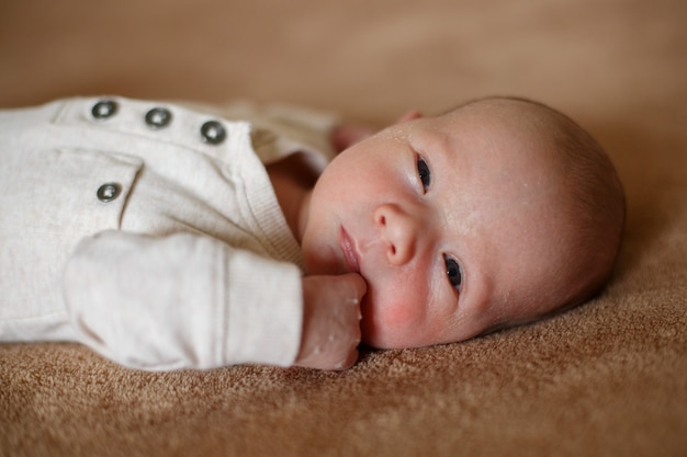 Recém-nascido saudável com um mês de idade na parede bege. pele de concha no rosto do recém-nascido. retrato de uma linda criança prematura. menino deitado em um lençol marrom macio na cama no quarto fechar.