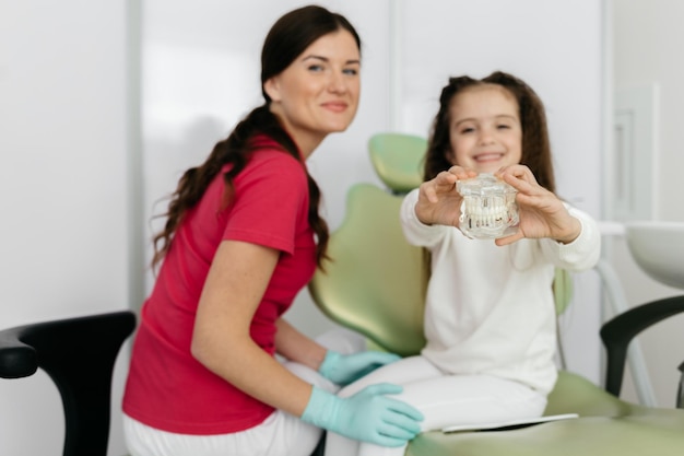 Recepção no dentista ajuda visual A menina tem nas mãos uma mandíbula artificial com dentes A criança expressa suas emoções ao olhar para o modelo