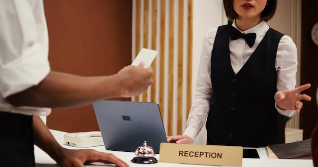 Foto recepcionista asiática oferecendo a parceiros de negócios afro-americanos em viagem de trabalho a chave do cartão de acesso ao quarto após finalizar o check-in. turistas terminando o processo de reserva, fechando a tomada