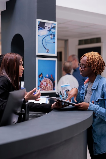 Recepcionista ayudando a la mujer en el mostrador de recepción, firmando documentos de informes médicos para recibir apoyo de seguros antes de la cita de control. Paciente rellenando el formulario de registro para hacer el examen.