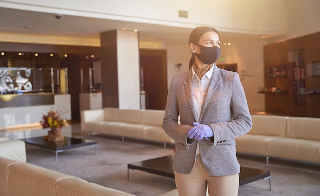 Recepcionista calma e elegante usando máscara de tecido e luvas de borracha durante o trabalho