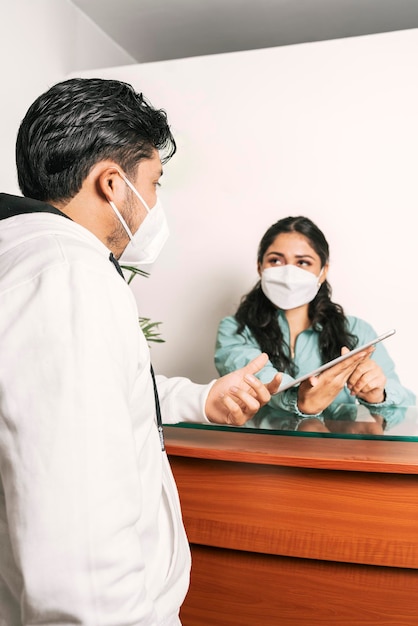 Recepcionista com máscara atendendo um homem em uma clínica odontológica