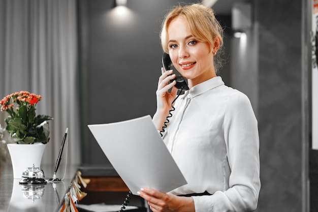 Recepcionista de hotel bonita e simpática falando ao telefone de perto