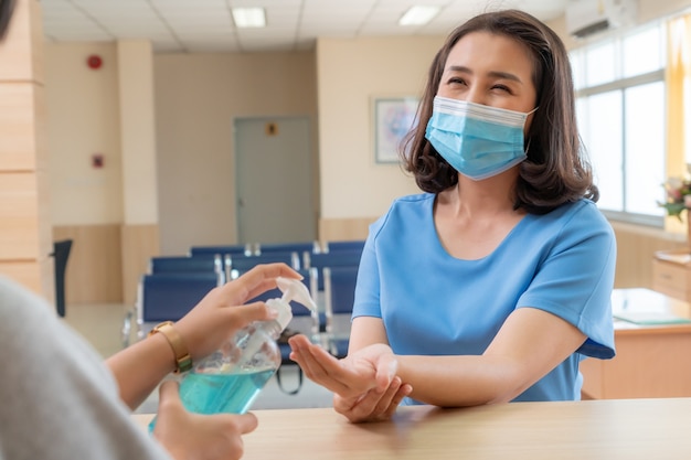 Recepcionista e convidado usando máscara facial na recepção enquanto conversam no escritório ou hospital